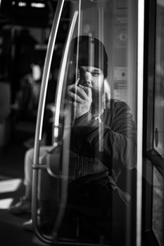 Woman looking out through a bus or train window, shot in black and white with window reflections.