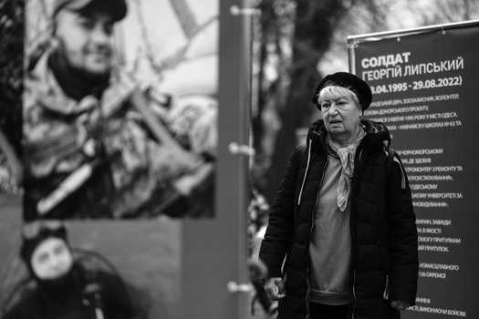 Man in black jacket stands before memorial plaques in black and white photograph.