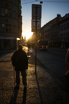 Person standing on a cobblestone street at sunset, backlit by warm golden light between historic buildings.