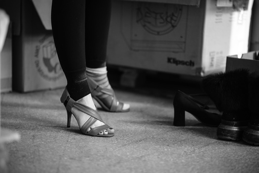 Close-up of dancer's feet in strappy heels and white socks on a carpeted floor.