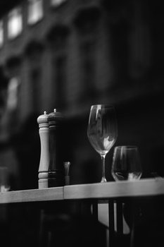 Wine glasses and bottle with pepper mill arranged on a table against a blurred dark architectural background.