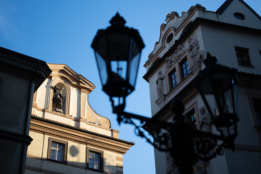 Ornate street lamps cast sharp shadows across historic building facades under clear blue sky.