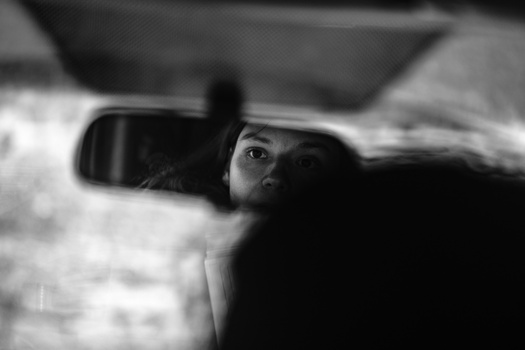 Person's face reflected in a car's side mirror, captured in black and white.