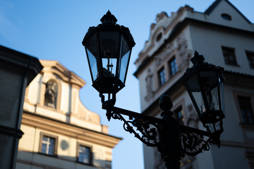 Silhouetted ornamental street lamps against historic European buildings in golden afternoon light.