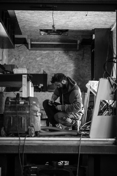 Photographer crouching in a studio workspace surrounded by equipment and materials.