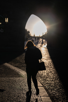 Silhouetted figure holding an umbrella on a cobblestone street at night, backlit by warm streetlights.