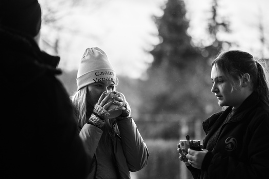 Three people in winter clothing holding warm beverages outdoors in black and white.