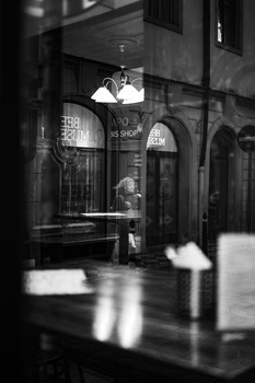 Rainy urban storefront at night with warm interior lighting glowing through arched windows.