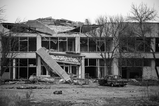 Severely damaged multi-story concrete building with blown-out windows and collapsed roof sections.