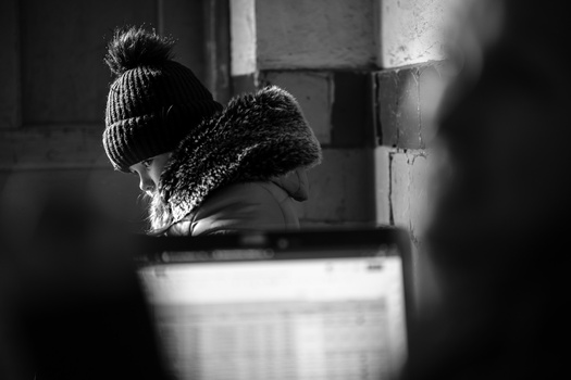 Person wearing a knit beanie and textured scarf in profile, shot in high-contrast black and white lighting.
