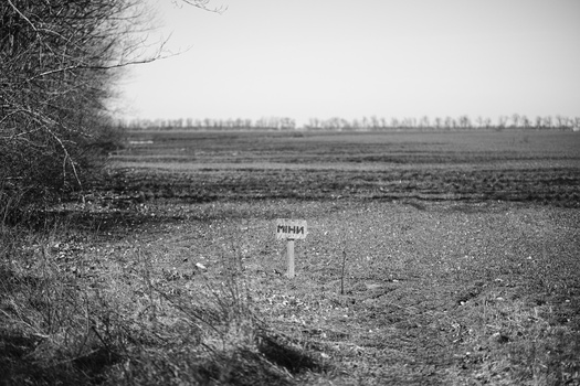 Small wooden marker sign in a sparse, plowed field under overcast sky.