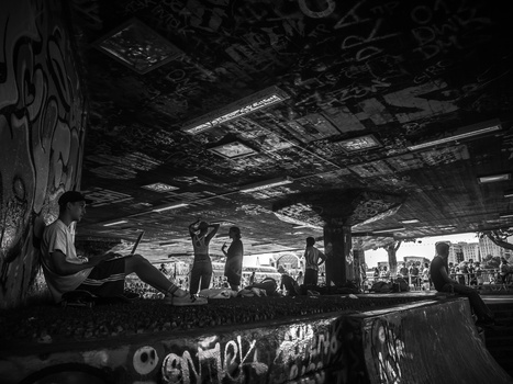 Person sitting on graffitied concrete ledge under an industrial underpass structure.