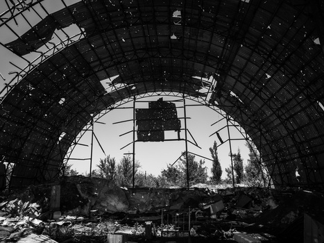 View through a massive arched industrial structure with skeletal framework, looking toward bare trees and overcast sky.
