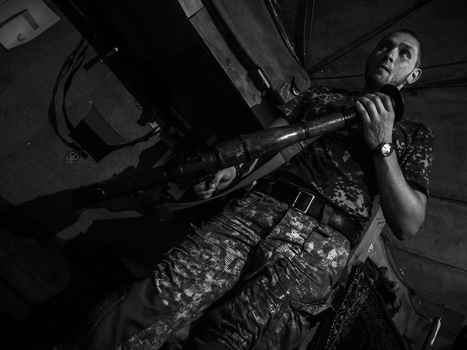 Soldier in camouflage uniform aiming rifle upward in black and white photograph.