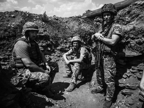 Four soldiers in military gear and helmets positioned in a rocky, excavated trench area during daytime.