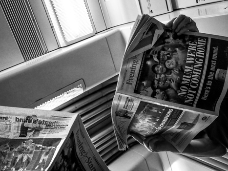 Black and white overhead shot of newspapers and magazines arranged on a striped surface near a window.