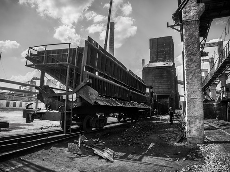 Industrial railway yard with a tilted dump truck on tracks beside concrete structures and buildings.