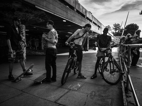 Group of cyclists and pedestrians gathered under a bridge overpass in an urban setting.