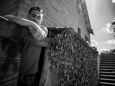 Man in work clothes holding a wooden plank against a brick building wall.