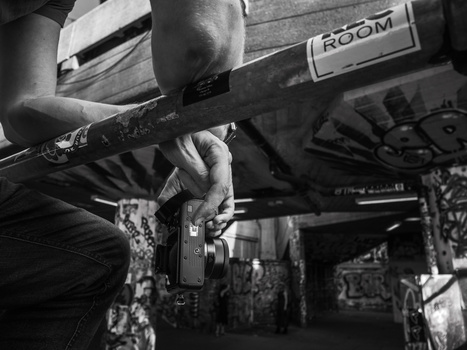 Photographer holding a vintage film camera under an airplane fuselage in black and white.