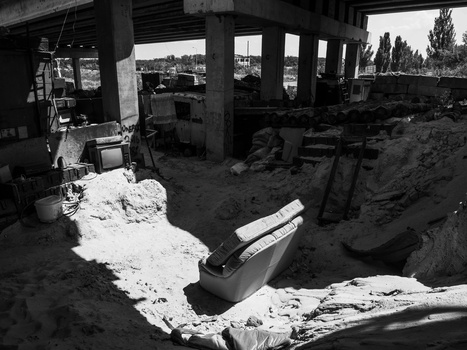 Black and white photograph of an industrial construction site beneath a concrete overpass with scattered materials and equipment.