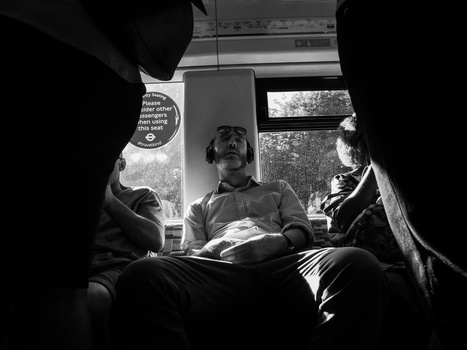 Three people seated in a bus or vehicle interior, shot in black and white from a low angle with strong contrast and window light.