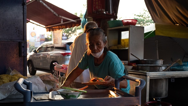 Street food vendor preparing a dish at an outdoor market stall during golden hour.