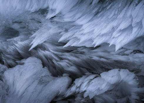 Frozen waterfall with layered ice formations and flowing water creating dynamic texture and movement.