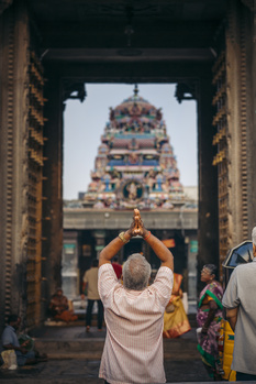 Person with hands raised toward ornate temple gopuram framed by golden doorway columns.