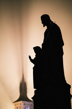 Silhouetted adult and child standing on a pedestal against a warm, glowing backdrop with a church spire visible.