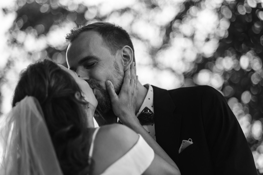 Groom touching bride's face tenderly during intimate wedding moment in black and white.