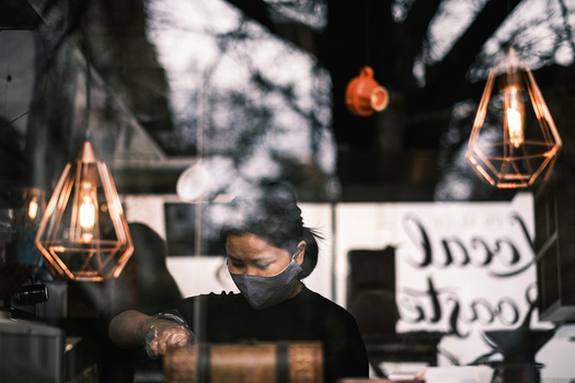 Person wearing a mask sitting indoors beneath hanging geometric copper pendant lights with warm filament bulbs.