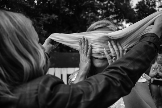 Two people's hands holding and adjusting flowing white fabric outdoors in black and white.