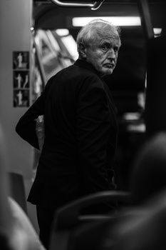 Older man in dark blazer looking over shoulder in black and white portrait.