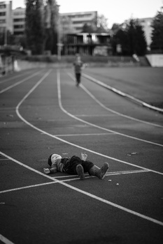 Person lying on a curved athletic track in an urban sports facility.
