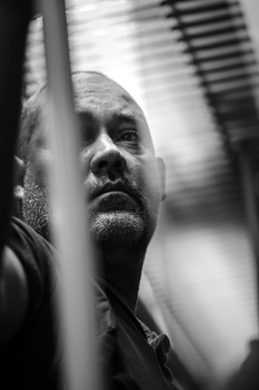 Black and white portrait of a man's face partially obscured by horizontal lines, looking upward with contemplative expression.