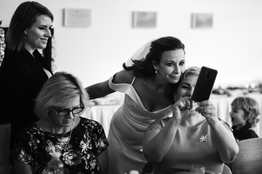 Group of people gathered indoors, with a woman in the center holding up a smartphone to capture a moment.