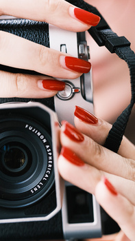 Hands with red nail polish holding a vintage film camera with black strap.