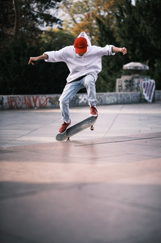 Skateboarder performing a kickflip trick on a concrete skate plaza with trees in the background.