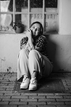 Person sitting against a wall with head resting on hand, wearing patterned sleeves, shot in black and white.