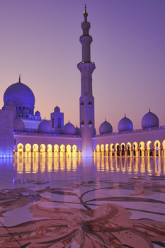 Illuminated mosque with ornate domes and tall minaret at dusk under purple twilight sky.