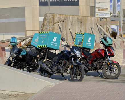 Three delivery motorcycles with turquoise insulated boxes parked in an urban setting.