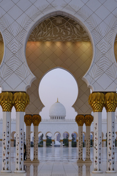 Symmetrical colonnade with ornate golden capitals framing a white domed structure in the distance.