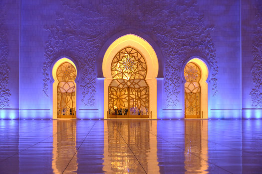 Three illuminated archways with intricate geometric lattice patterns reflected on a polished floor.