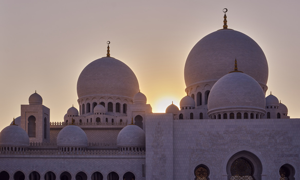 Islamic mosque with multiple domes silhouetted against golden sunset sky.