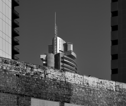 Modern high-rise building with antenna viewed through concrete structure in black and white.