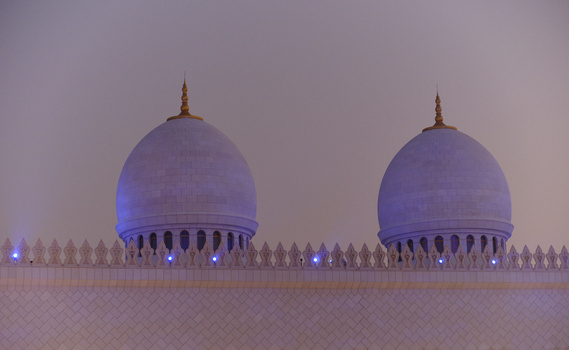 Two domed structures with blue illumination against a twilight sky, separated by an ornate fence.