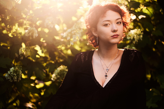 Woman in black top gazing upward amid glowing yellow foliage in natural light.