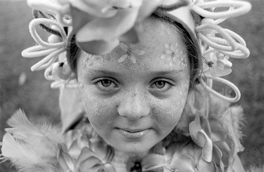 Young child with curled hair ribbons looking directly at camera with gentle expression in black and white portrait.