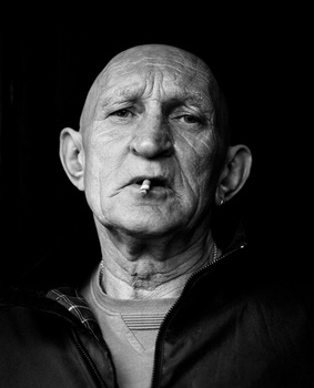 Black and white portrait of an older bald man with a stern expression against a dark background.